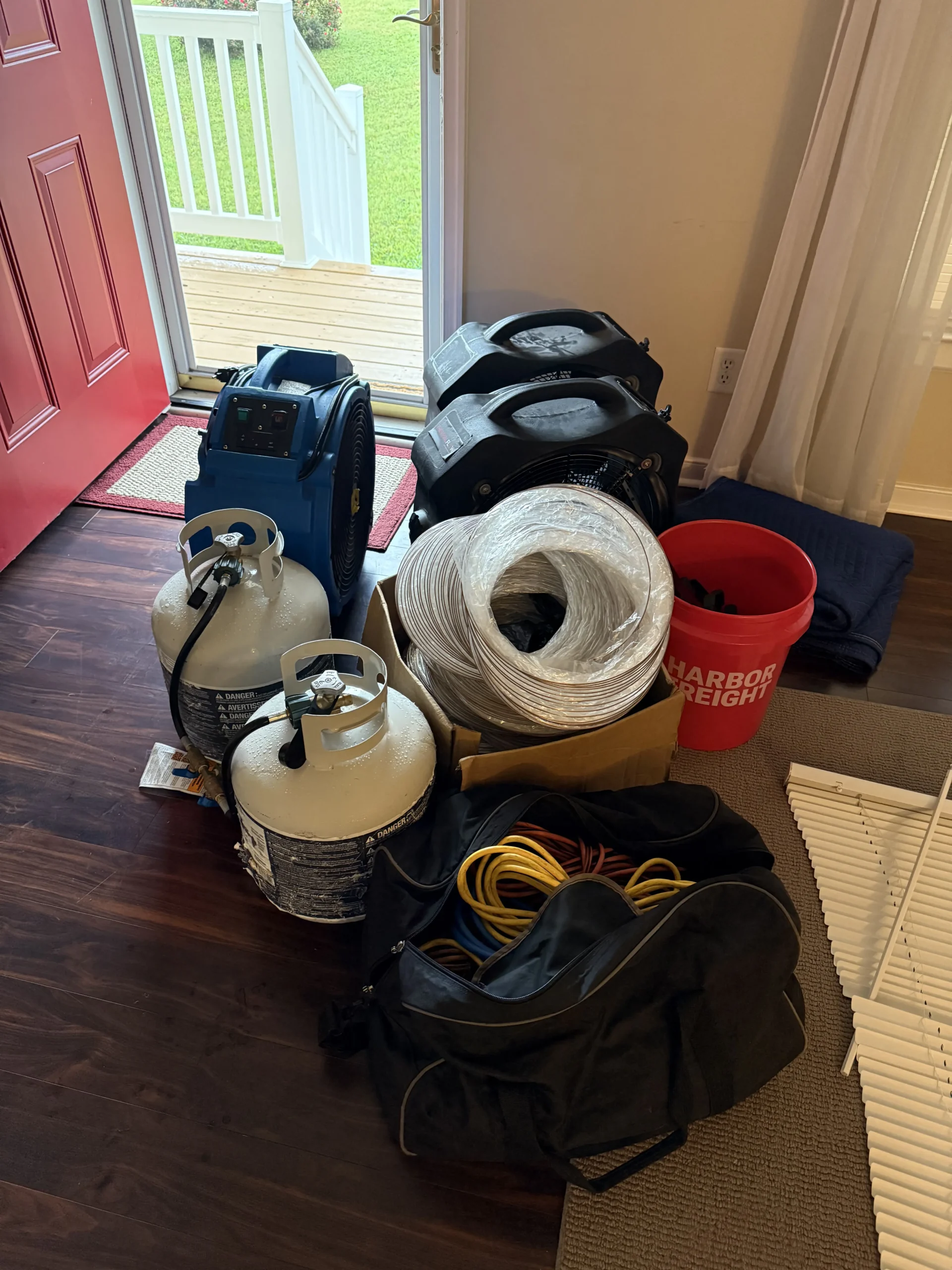 This is an indoor photograph of a collection of bed bug treatment items gathered on a dark wood floor near an open doorway.