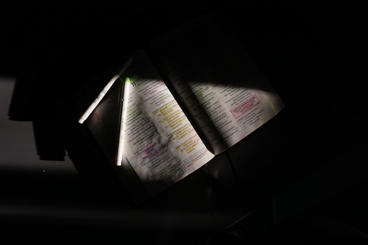 A bright flashlight, magnifying glass, thin card, screwdriver, zip-top bags, clear tape, gloves, a notepad, and a hard-sided plastic bin arranged on a hard floor beside a bed, with trash bags and a laundry bag nearby for containing bedding and clothing