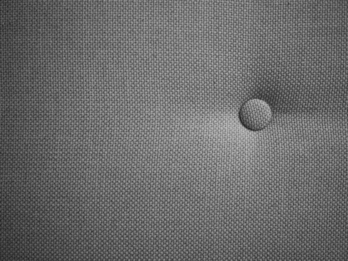 A close-up inspection scene of a mattress corner and box spring with a flashlight beam revealing tiny dark ink-like spots along the seam, a few pale shed skins near the stitching, and a bed frame joint with visible cracks beside the bed