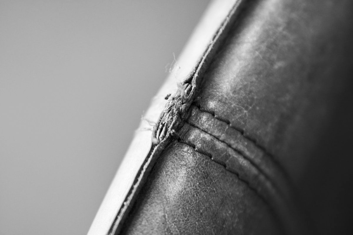 A close-up bedroom scene showing a mattress corner with tiny black specks along the seam, a pale shed insect skin near the piping, and a few rusty smears on a white sheet beside the bed frame