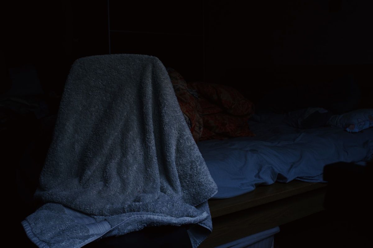 A close-up bedroom scene with a mattress seam pulled back for inspection, a flashlight shining along the edge of the bed, and a small invoice or receipt on a nightstand showing the idea of a low-cost home visit compared with a larger repair bill in the background