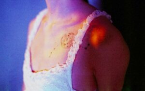 A bare shoulder and upper arm showing several tiny red bite marks grouped in a short straight line and a nearby zigzag pattern, with the skin slightly irritated and uneven in size