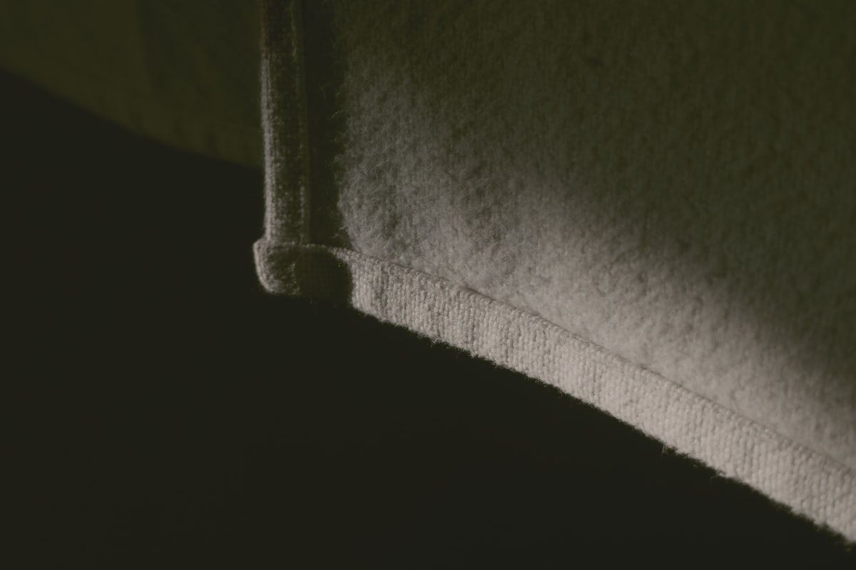 A flashlight beam shining across the edge of a mattress, revealing tiny dark specks, shed skins, and a few small blood spots along the seam near a bed frame and headboard
