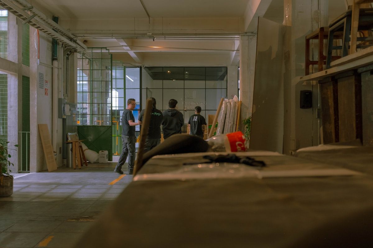 A residential entryway scene showing three inspection approaches: a pest inspector examining a mattress seam with a flashlight, a trained detection dog sniffing along a baseboard near furniture, and a homeowner reviewing a service estimate sheet beside them as they discuss options